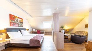 A modern bedroom with a large bed, a desk, a chair, and a sofa. - Hotel Alexander (Basel)