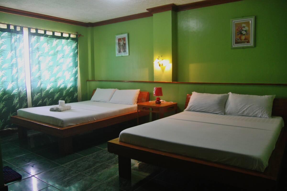 Una habitación con dos camas individuales, una mesita de noche con lámpara y una ventana con cortinas.