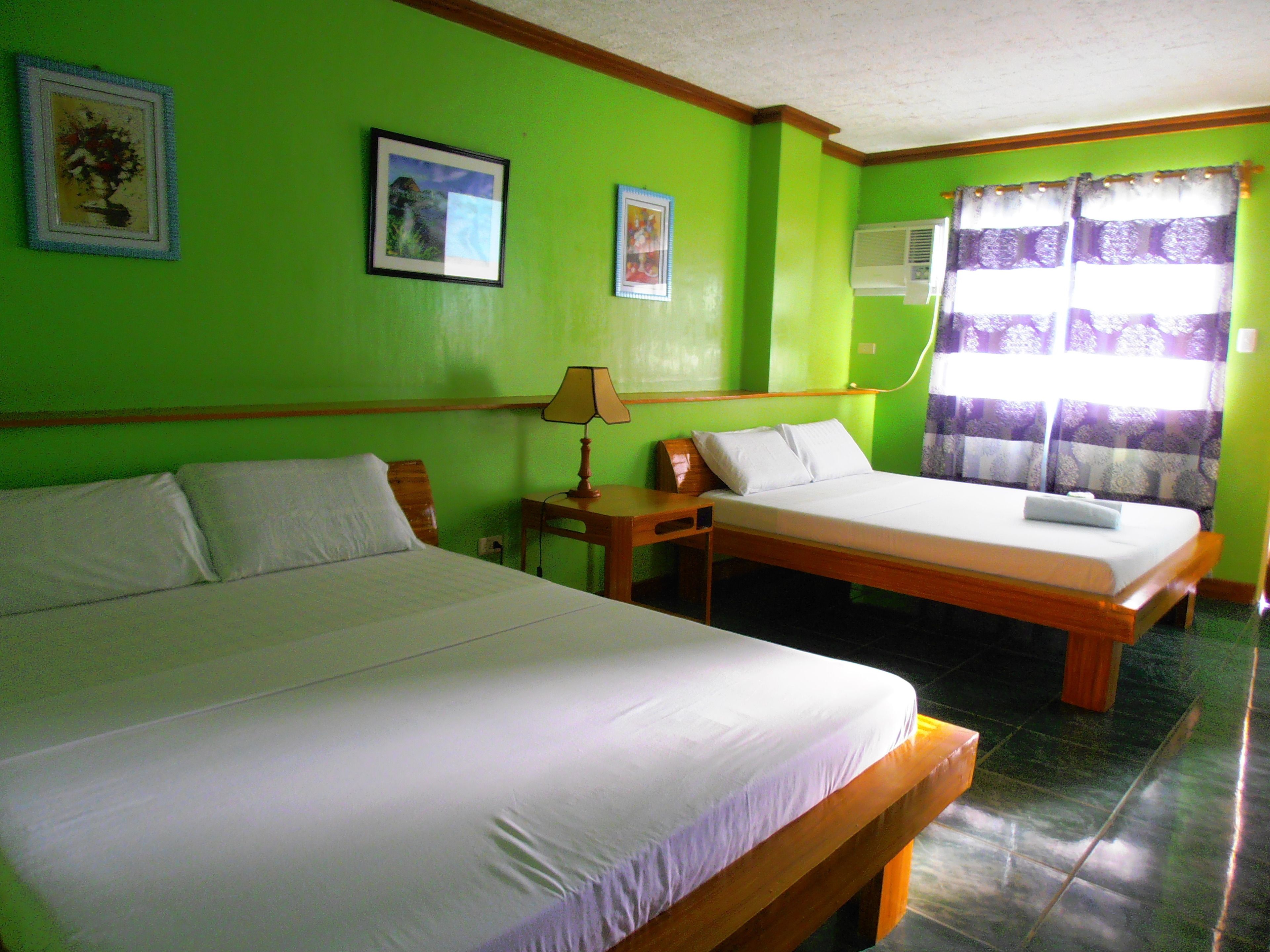 A room with two beds, a nightstand, a lamp, and a window with curtains.