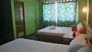 Una habitación con una cama, una mesita de noche con lámpara, un ventilador y una ventana con cortinas estampadas.