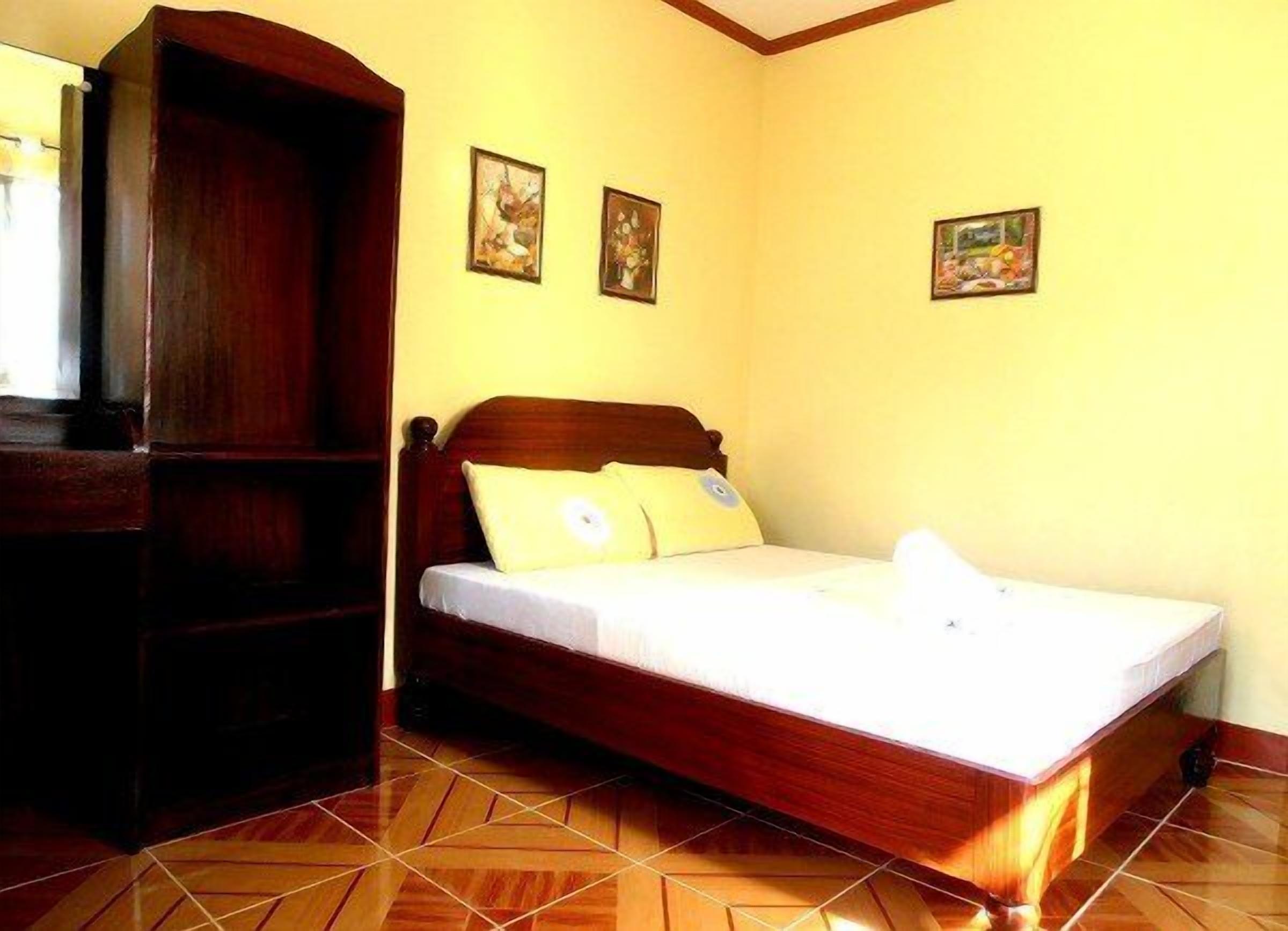A bedroom with a wooden bed, a wardrobe, and three framed pictures on the wall.