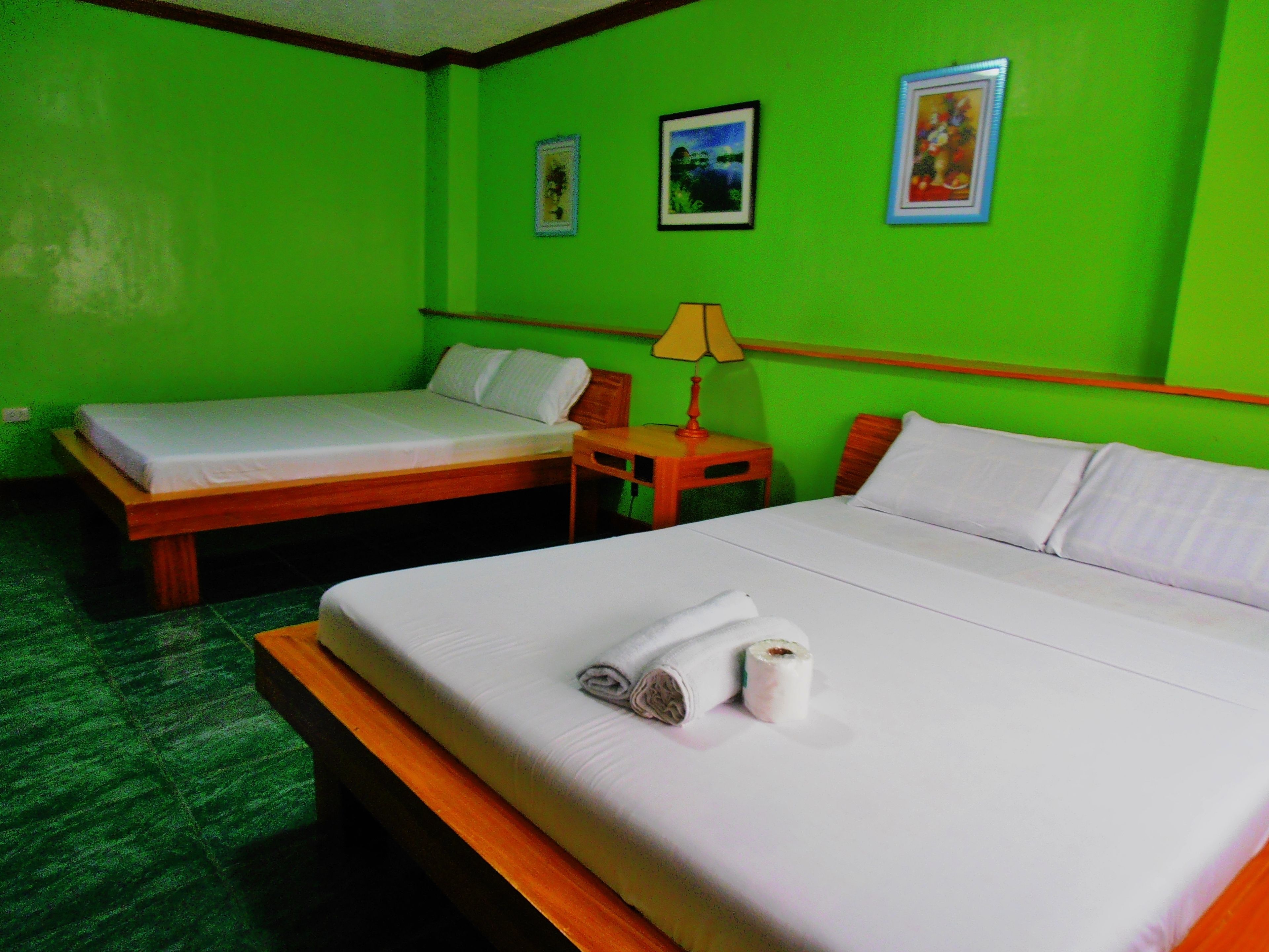 A hotel room with two beds, a wooden headboard, a nightstand with a lamp, and green walls.