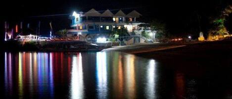 Un edificio grande de varios pisos con un balcón que da a una masa de agua, reflejando luces.