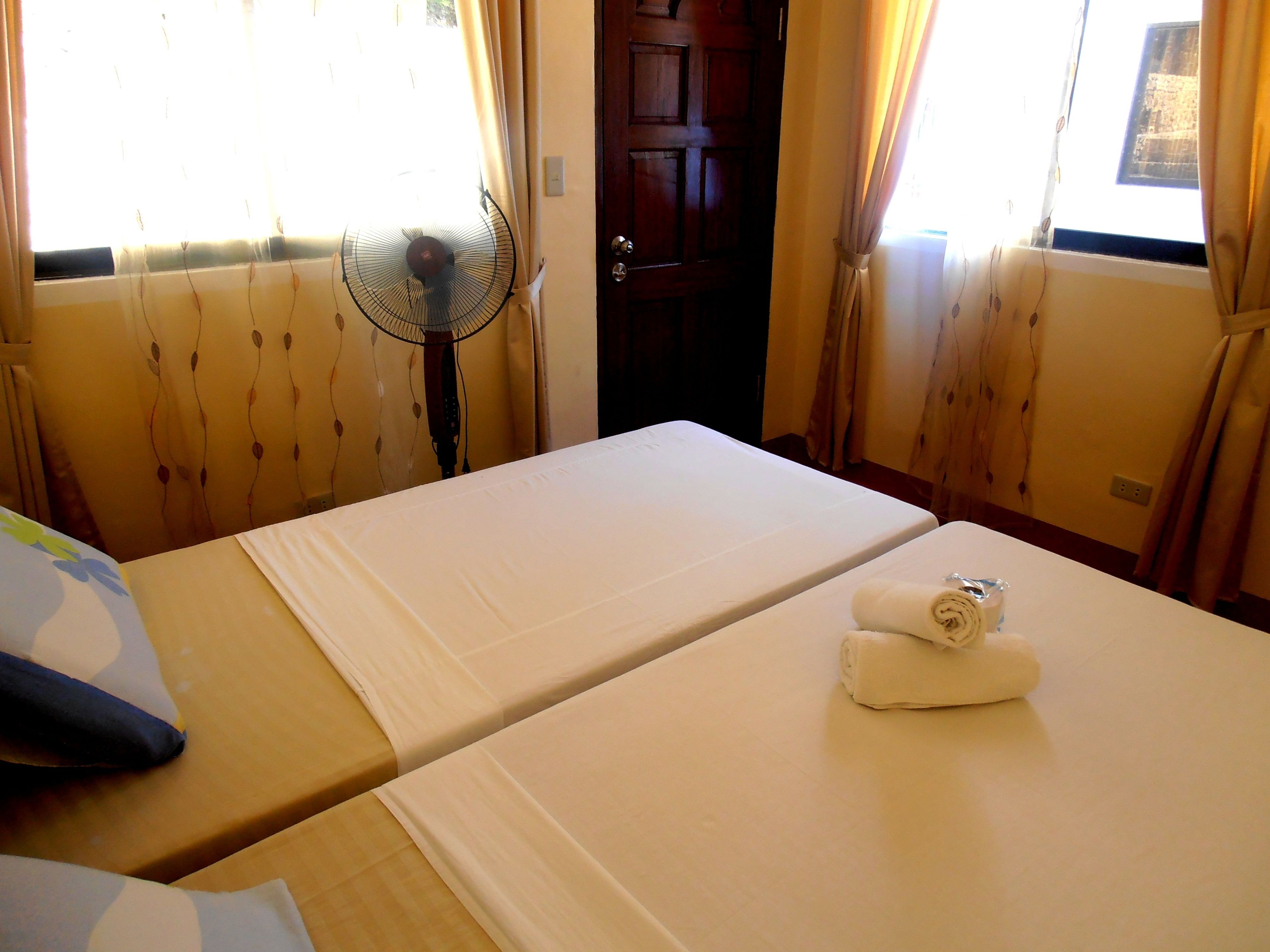 A hotel room with two beds, a fan, and curtains.