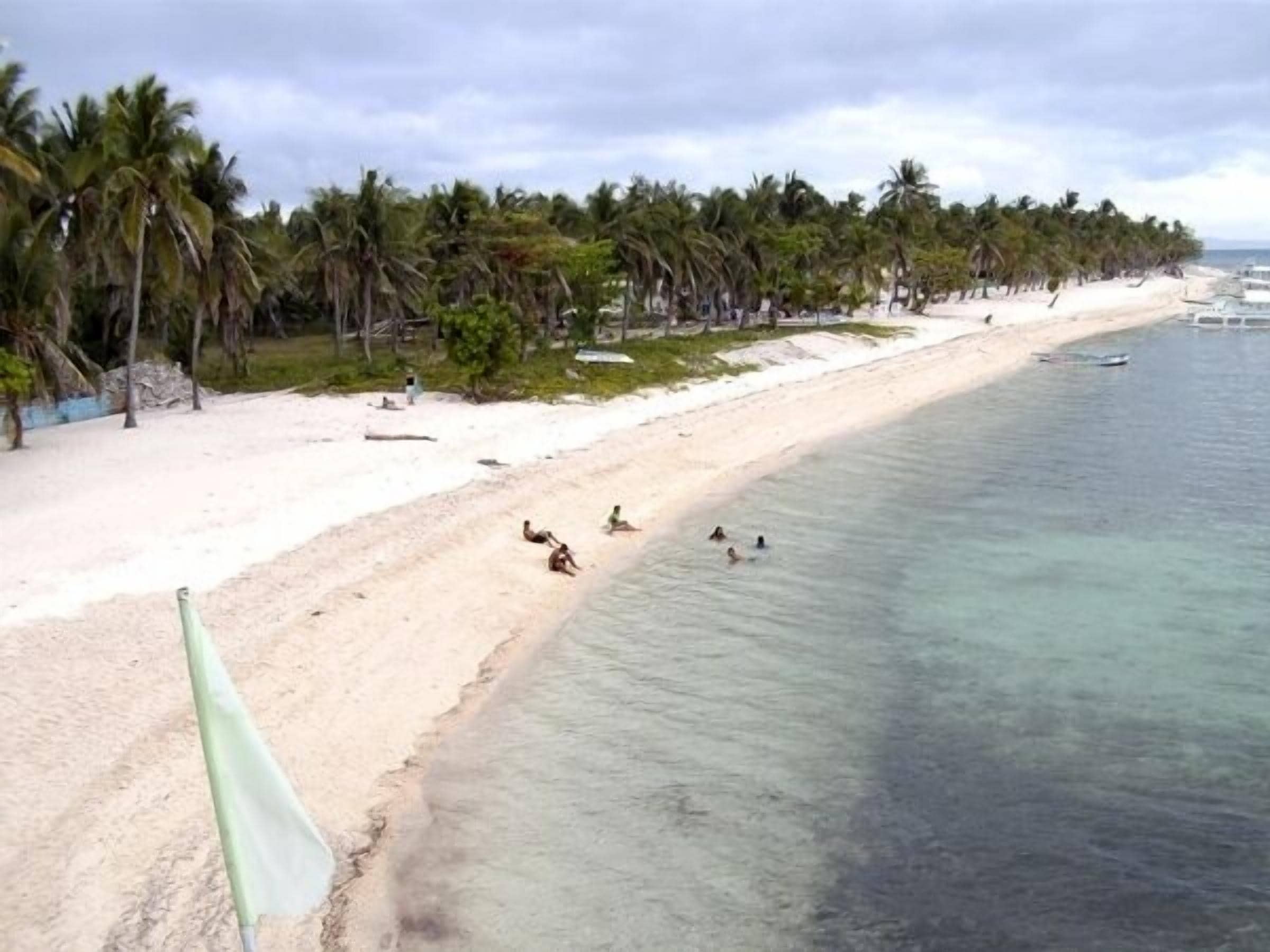A beach with clear turquoise water, palm trees, and a few people swimming.