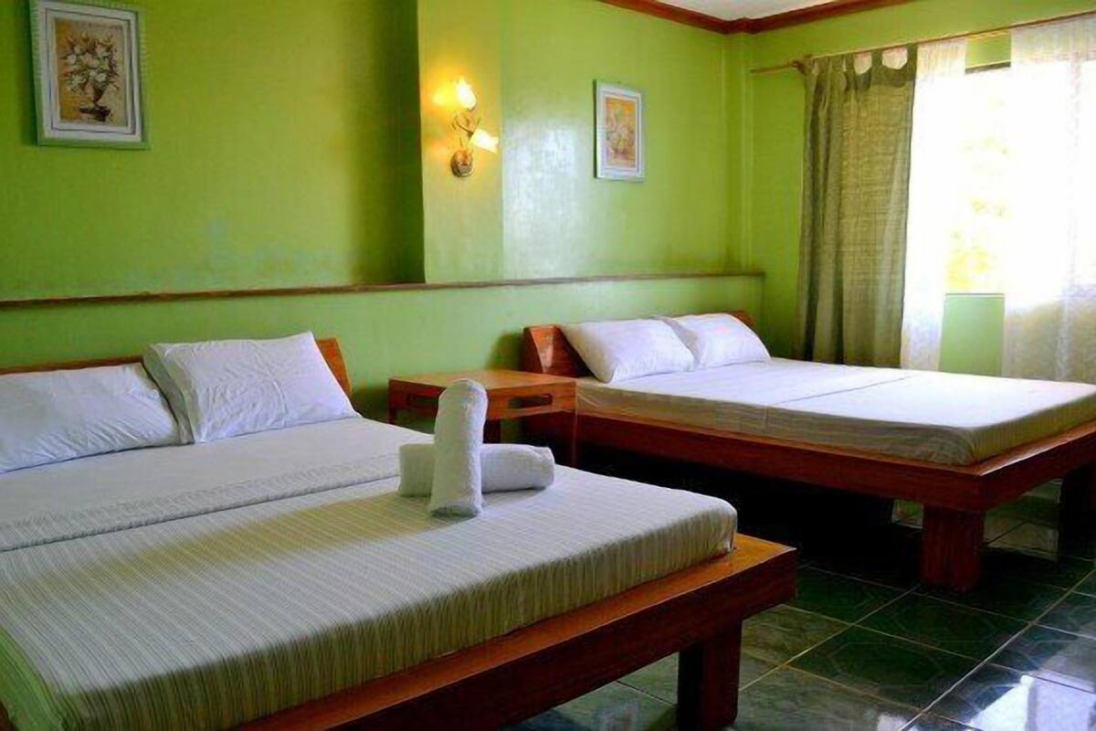 Habitación con dos camas, paredes verdes y una ventana con cortinas.