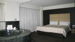 A modern hotel room with a large bed, a built-in bathtub, and a large window with curtains.