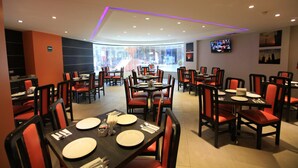 A restaurant with round tables, red chairs, and a TV on the wall.