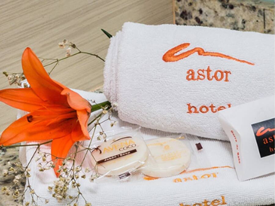 Una toalla de hotel con el logotipo 'Avena Coco', una flor naranja brillante y una pequeña botella sobre una encimera de granito.