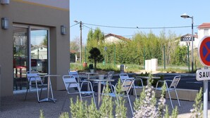 An outdoor seating area with metal chairs and tables, a building entrance, and a 'no parking' sign. - The Originals ACCESS Tendance Hôtel (Andrezieux-Boutheon)