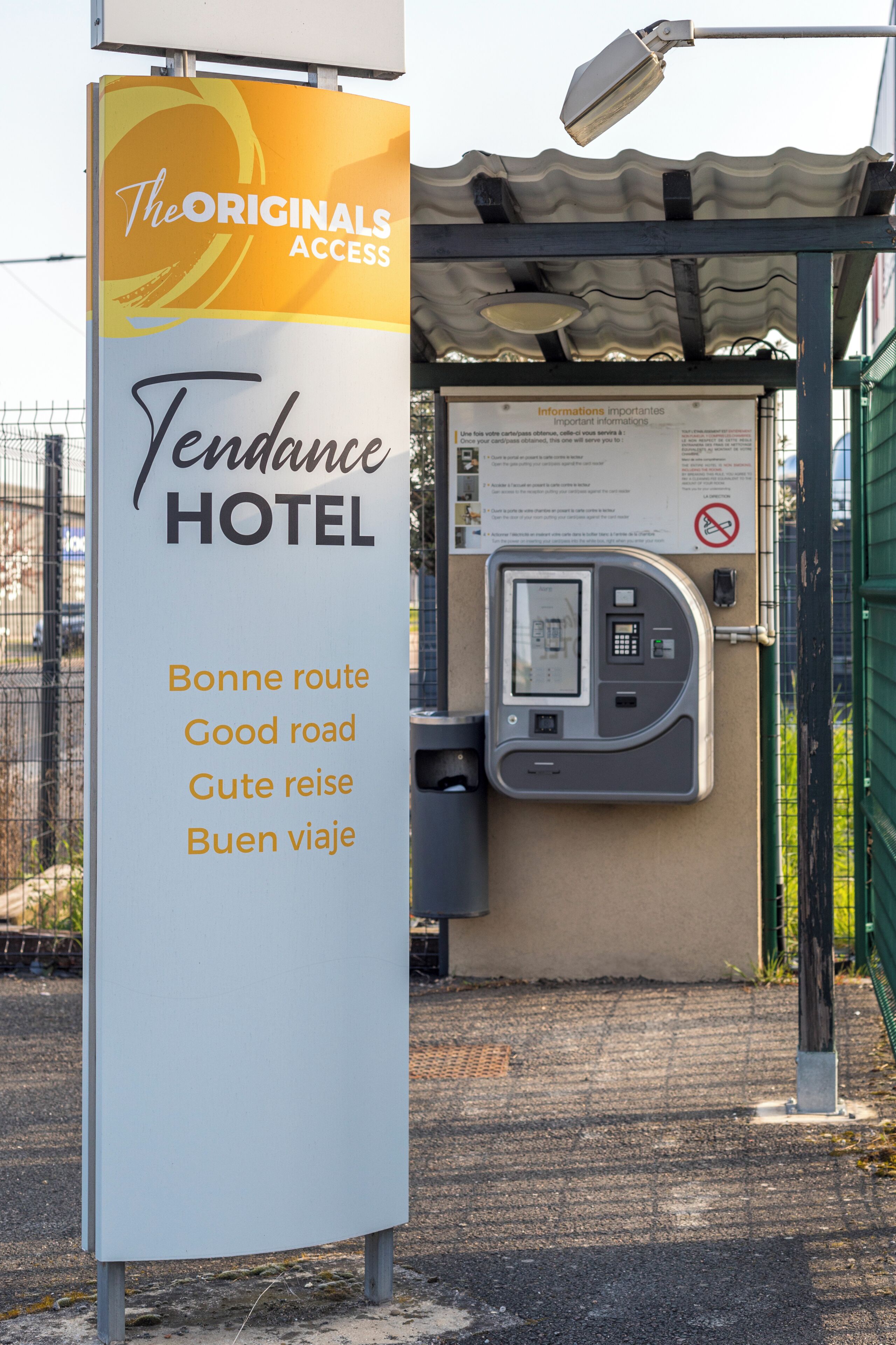 A sign for The Originals Access Tendance Hotel with a payment kiosk and a no-smoking sign.