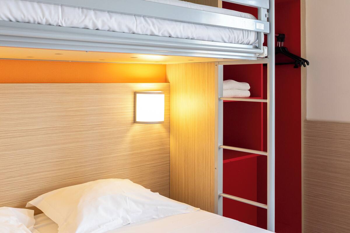 Un lit superposé avec une tête de lit en bois, une armoire rouge et une petite lampe de chevet.