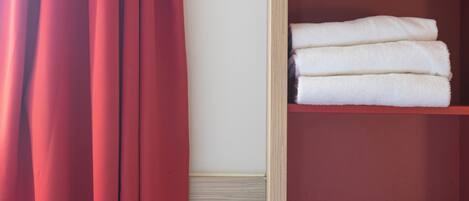 A room with a red curtain, a wooden shelf with folded white towels, and a red shelf unit.