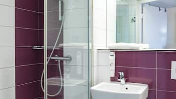 Ein modernes Badezimmer mit einer gläsernen Duschkabine, einem weißen Waschbecken und einem Spiegel darüber.