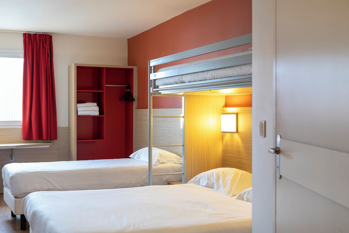 Hotellihuone, jossa on kaksi sänkyä, punainen vaatekaappi ja ikkuna, jossa on punaiset verhot.