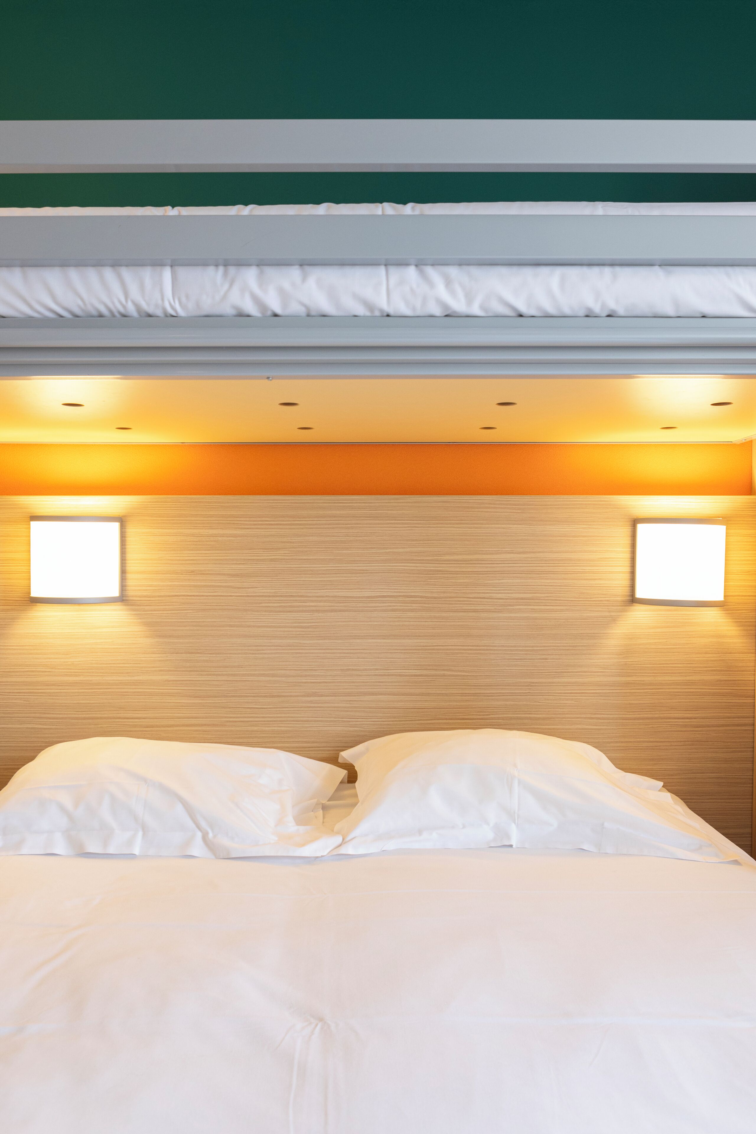 A hotel room with a bed, two bedside lamps, and a wooden headboard.