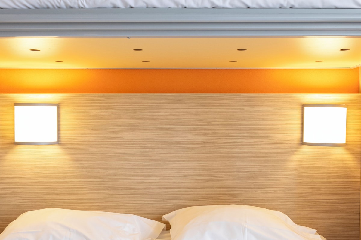 Hotellihuone, jossa on sänky, kaksi yöpöytälamppua ja puinen sängynpääty.