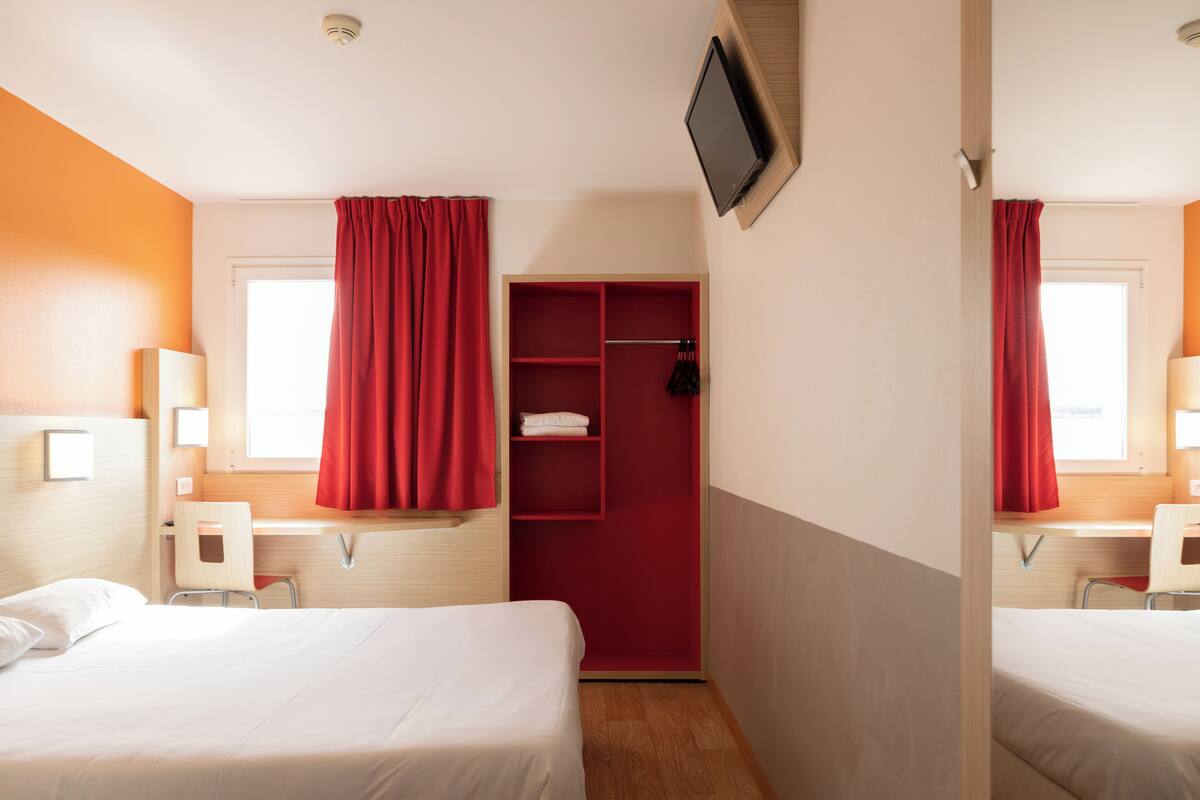 Une chambre d’hôtel avec deux lits, une télévision, un bureau et une armoire rouge.