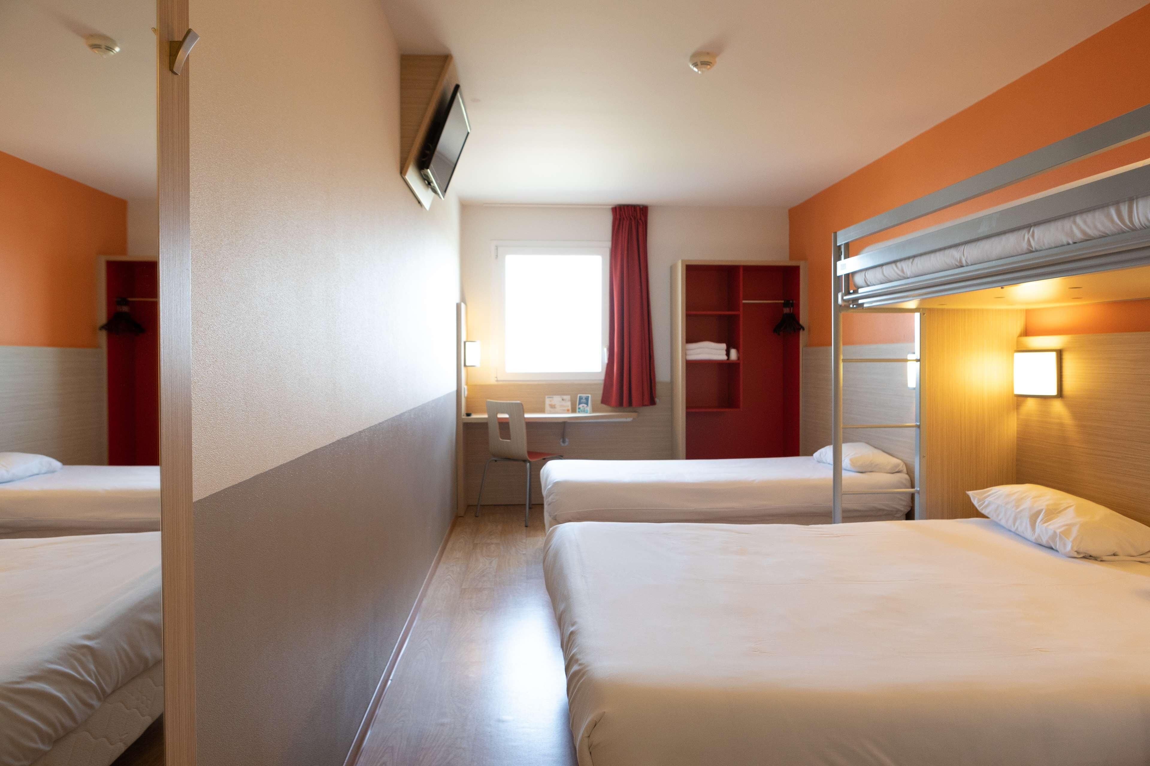 Une chambre d’hôtel avec deux lits, un bureau, une chaise, une télévision et une fenêtre avec des rideaux.