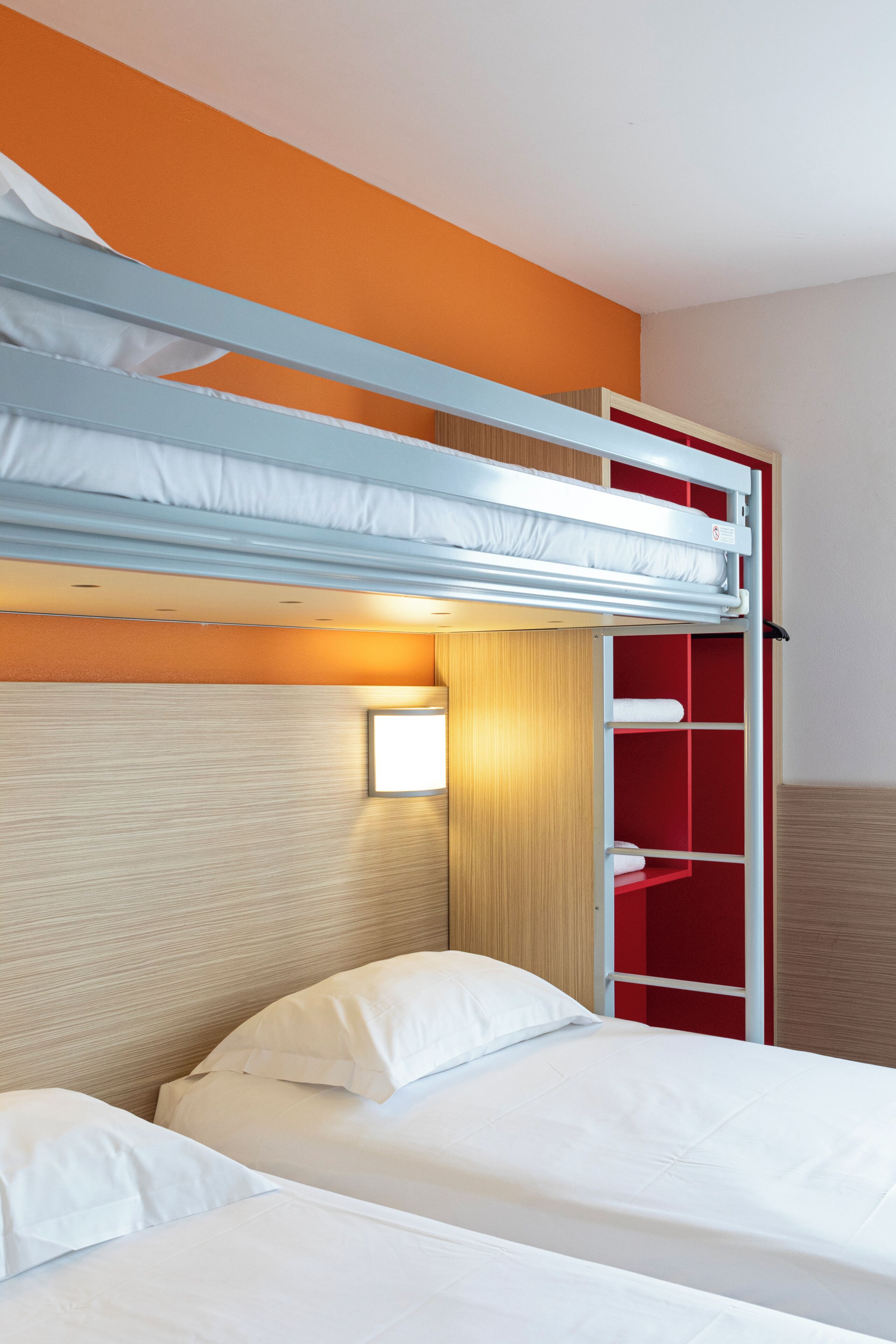 Un lit superposé aux couleurs rouge et blanc, une tête de lit dotée d’un luminaire et un mur recouvert de panneaux en bois.