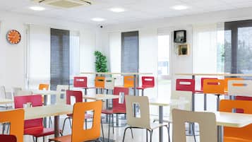 Una cafetería con mesas y sillas, un reloj y ventanas con persianas.