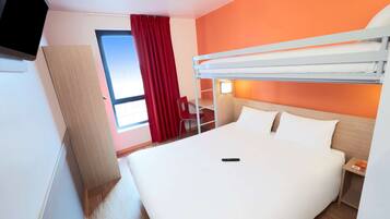 A hotel room with a bunk bed, a desk with a chair, a TV, and a window with red curtains.