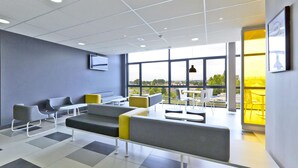 A modern waiting area with seating, a flat-screen TV, and large windows offering a view of the outdoors. - Hôtel Première Classe Thionville (Thionville)