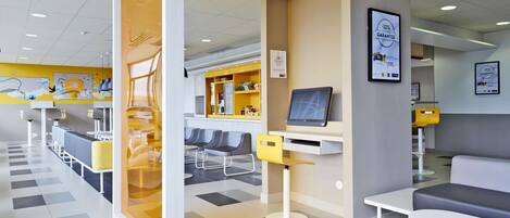 Un hall d’hôtel moderne comprenant un comptoir d’enregistrement, des espaces de détente et un bureau d’accueil.