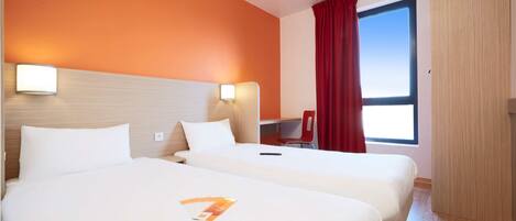 Habitación de hotel con dos camas, un escritorio, una silla y una ventana con cortinas.