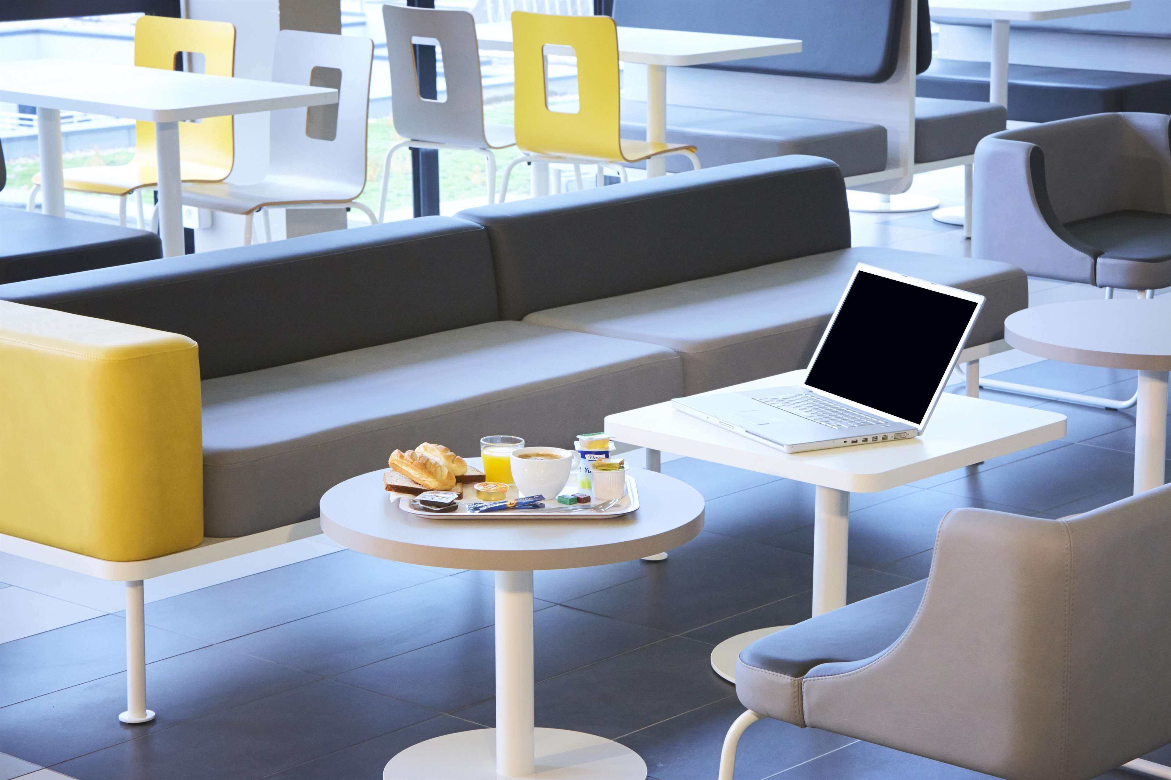 Un café moderne avec un ordinateur portable sur une table, un plateau contenant des articles pour le petit-déjeuner et des sièges confortables.