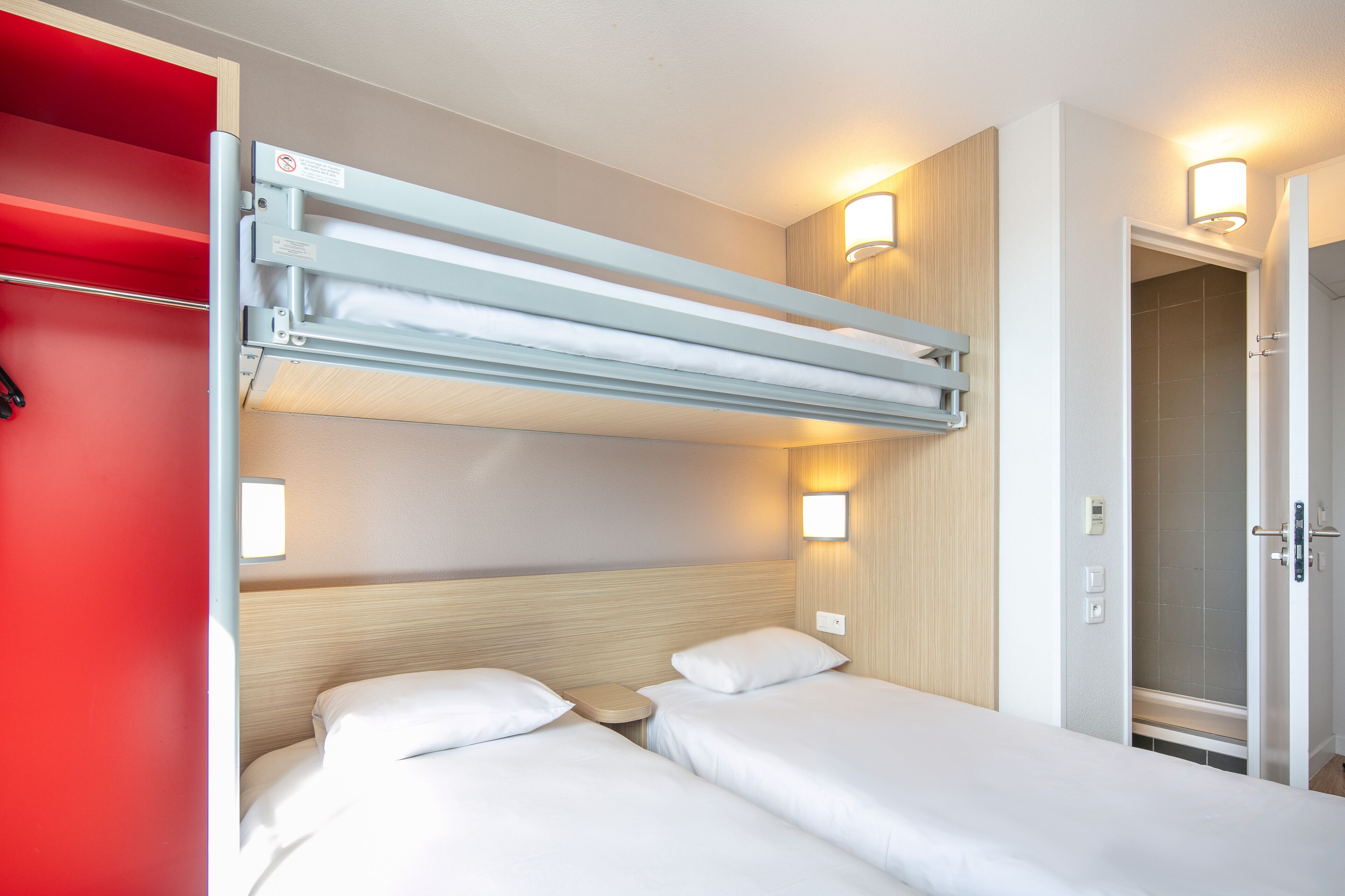 Ein Hotelzimmer mit zwei Betten, einer roten Wand und einer Deckenleuchte.