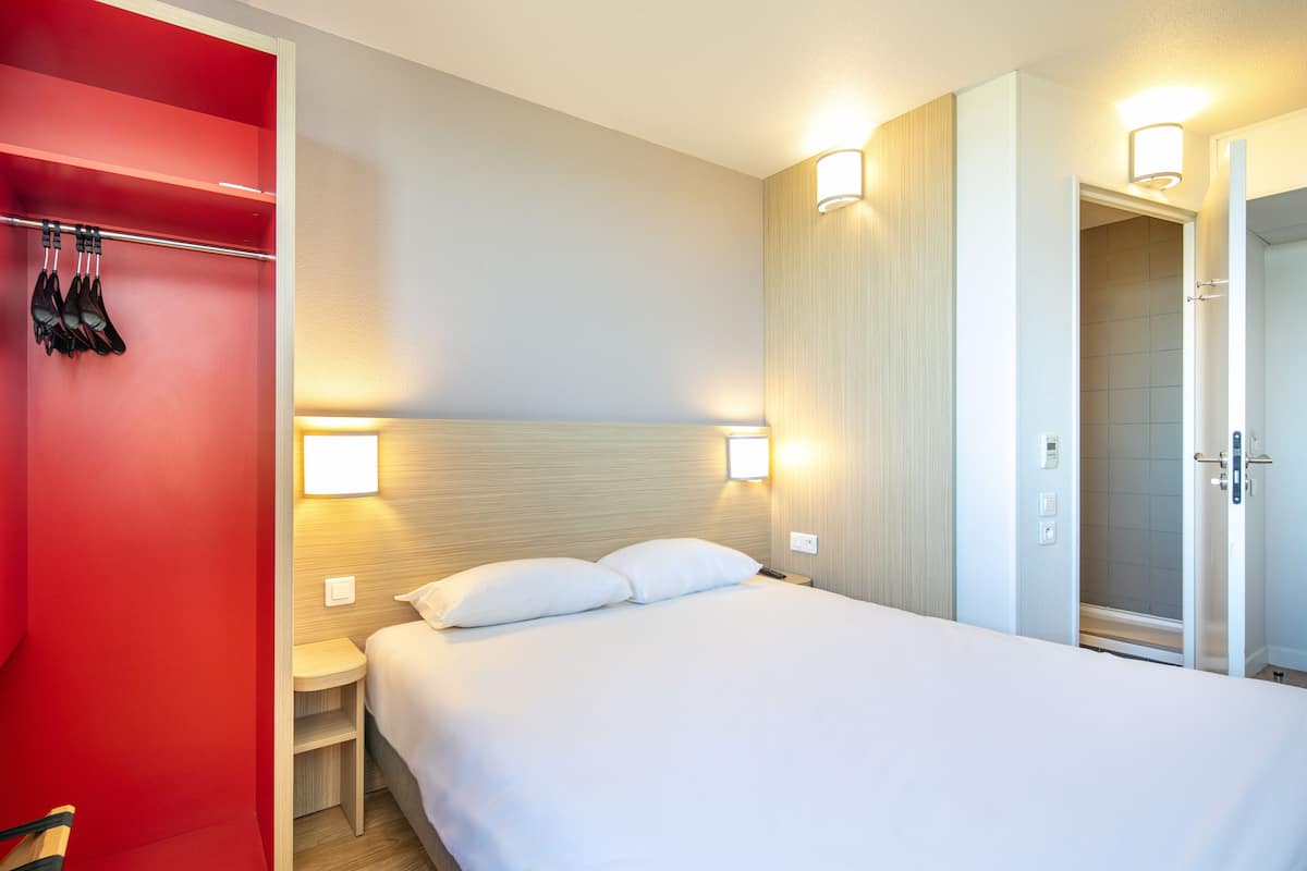 A hotel room with a bed, a red closet, and a shower area.