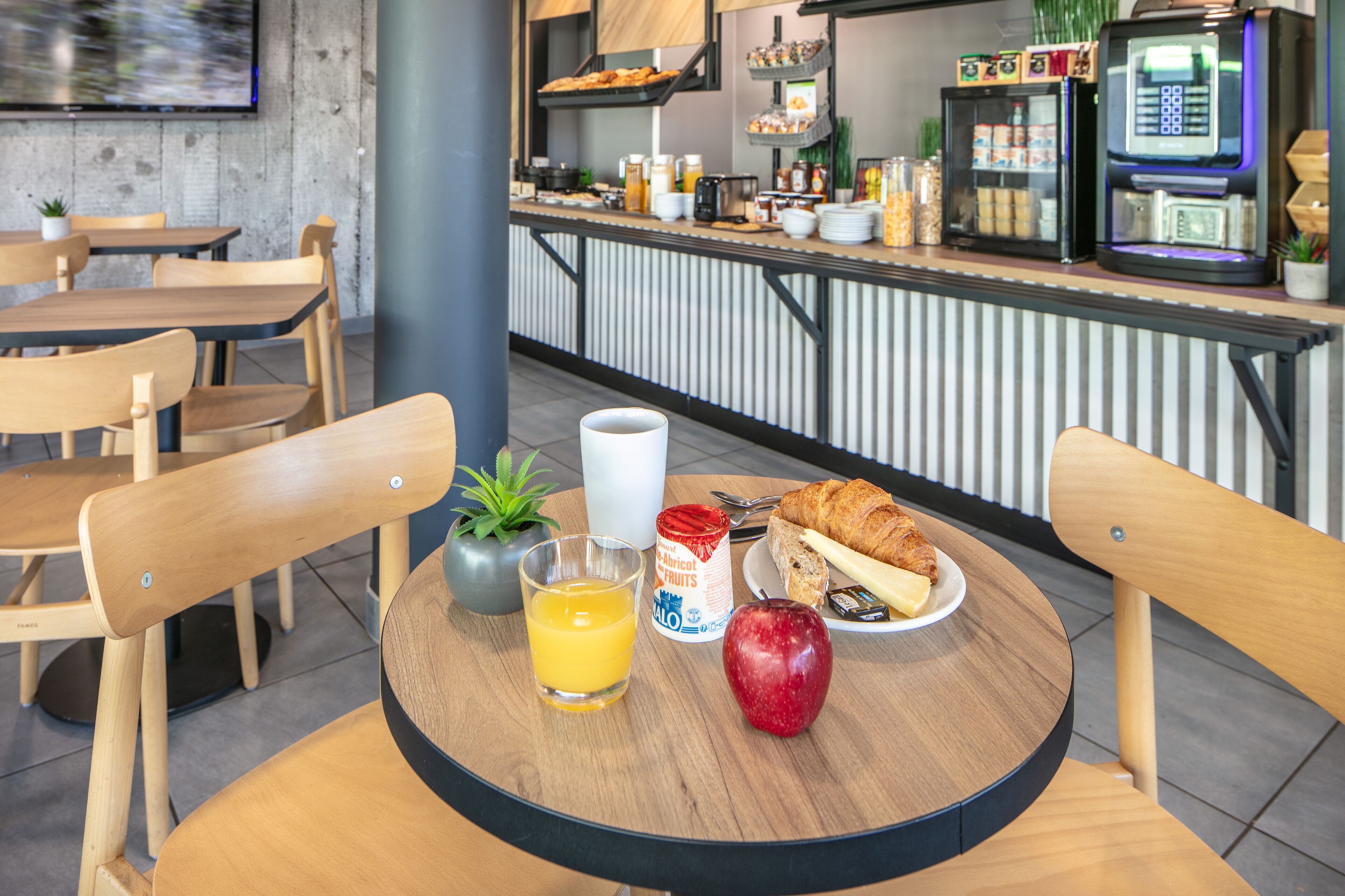 Une table mise pour le petit-déjeuner, avec une table, des chaises, une boisson, un croissant et un fruit.