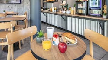 Une table mise pour le petit-déjeuner, avec une table, des chaises, une boisson, un croissant et un fruit.