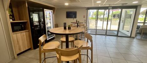 A modern indoor space with a round table and four chairs, a vending machine, and a microwave.