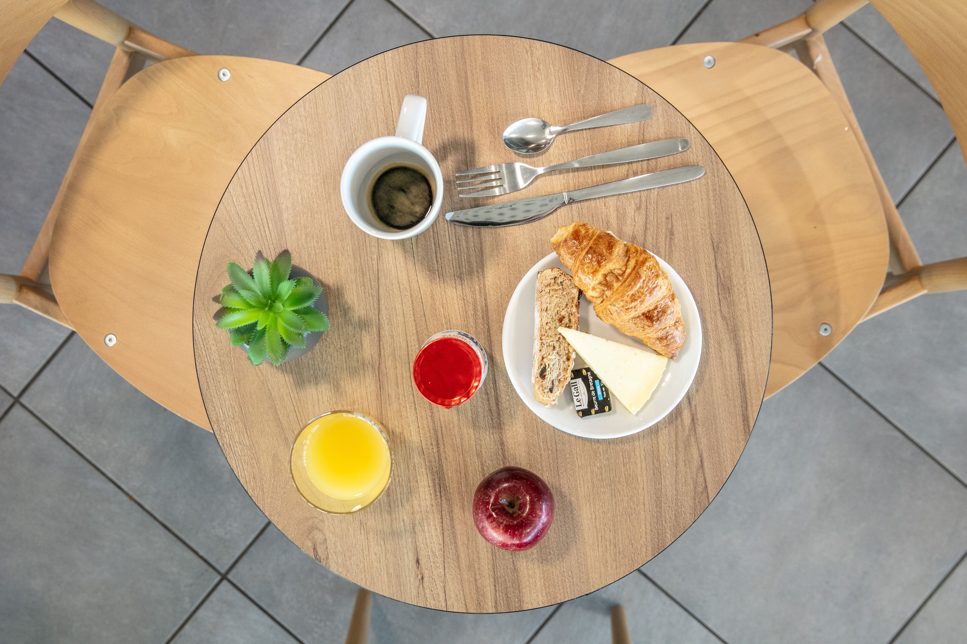 Een ronde houten tafel met een bord eten, een kop koffie, een glas sap en een kleine plant.