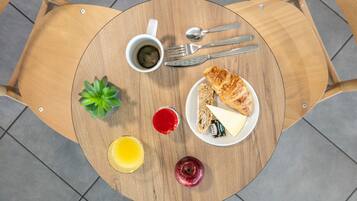 Een ronde houten tafel met een bord eten, een kop koffie, een glas sap en een kleine plant.
