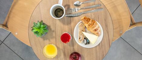 A round wooden table with a plate of food, a cup of coffee, a glass of juice, and a small plant.