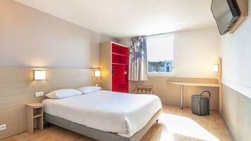 Een moderne hotelkamer met een bed, een rode garderobe, een klein tafeltje, een stoel, een aan de muur bevestigde televisie en een raam met uitzicht.