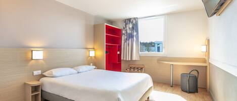 A modern hotel room with a bed, a red wardrobe, a small table, a chair, a TV mounted on the wall, and a window with a view.