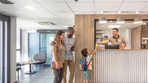 A modern reception area with a wooden reception desk, a seating area with a round table, and a glass partition. - B&B HOTEL Lyon Aéroport St Quentin Fallavier (Saint-Quentin-Fallavier)