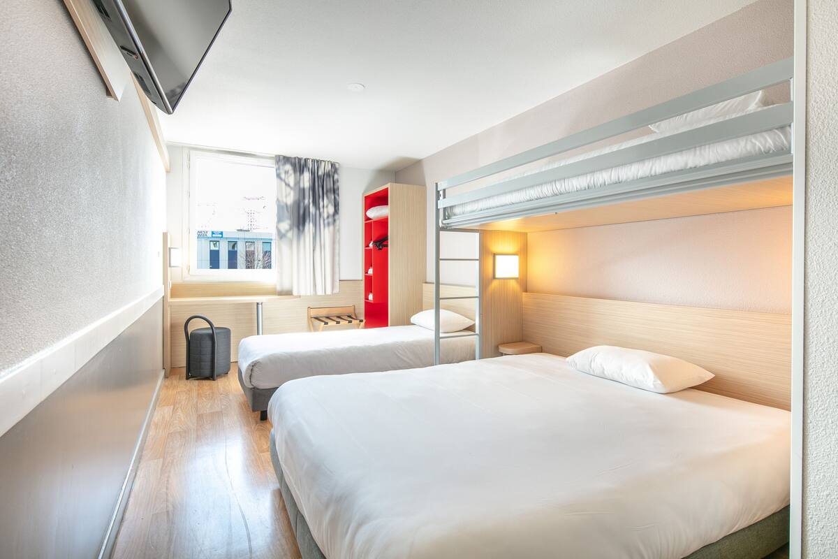 A hotel room with two beds, a red cabinet, a window with curtains, and a TV mounted on the wall.
