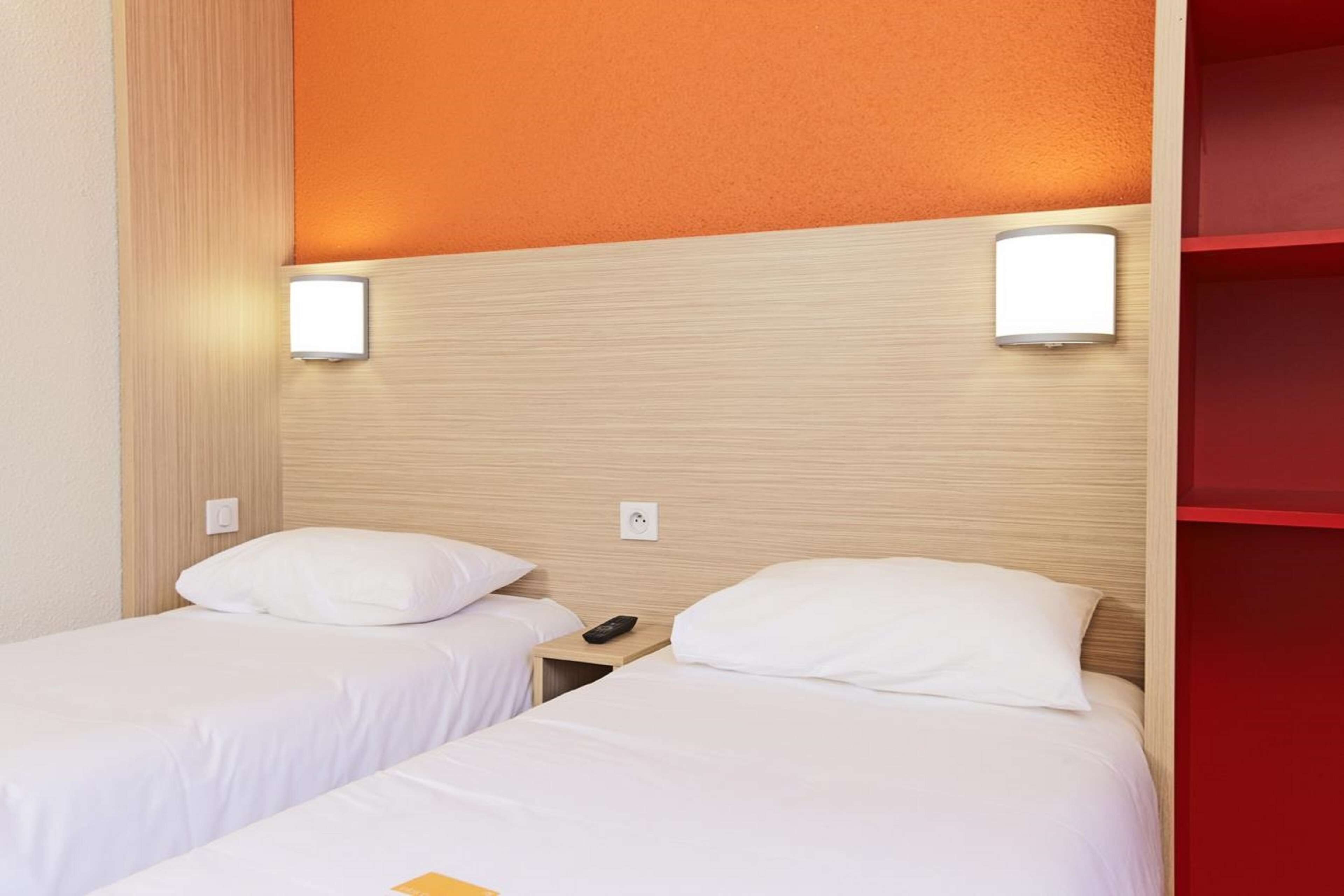 Une chambre d’hôtel avec deux lits simples, chacun doté d’un matelas et d’un oreiller blancs, d’une tête de lit en bois et d’une table de chevet avec une télécommande.