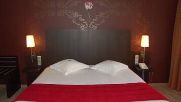 A hotel room with a large bed, two bedside lamps, a floral wall design, and a red bedspread.
