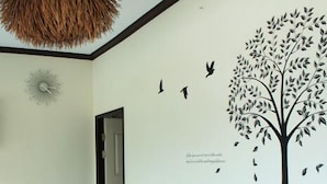 A room with a wooden sofa, a wall mural of a tree with birds, and a door leading to another room. - Garden Home Resort (Koh Samui)