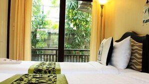 A hotel room with two beds, a balcony, and a view of greenery. - Garden Home Resort (Koh Samui)