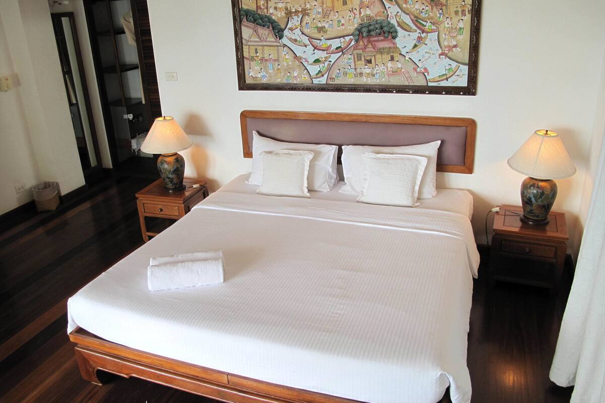 A hotel room with a large bed, two bedside tables with lamps, a headboard, and a wall-mounted painting.