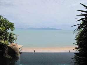 A clear view of a beach with a pool in the foreground, a sandy shore, and mountains in the distance. - Grand Villa La Perla (Koh Samui)