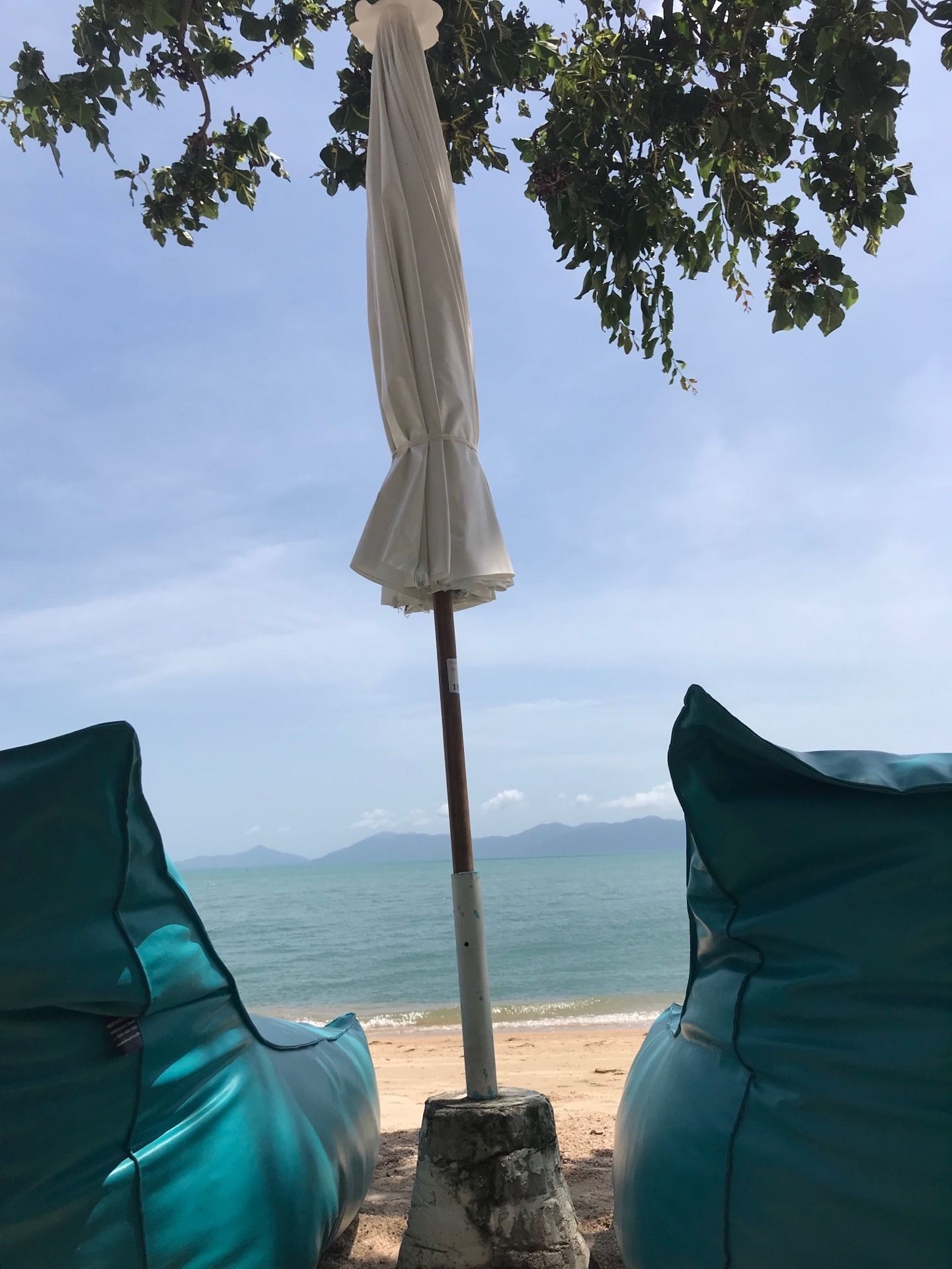 Une vue sur la plage avec un parasol blanc et deux chaises longues turquoise.