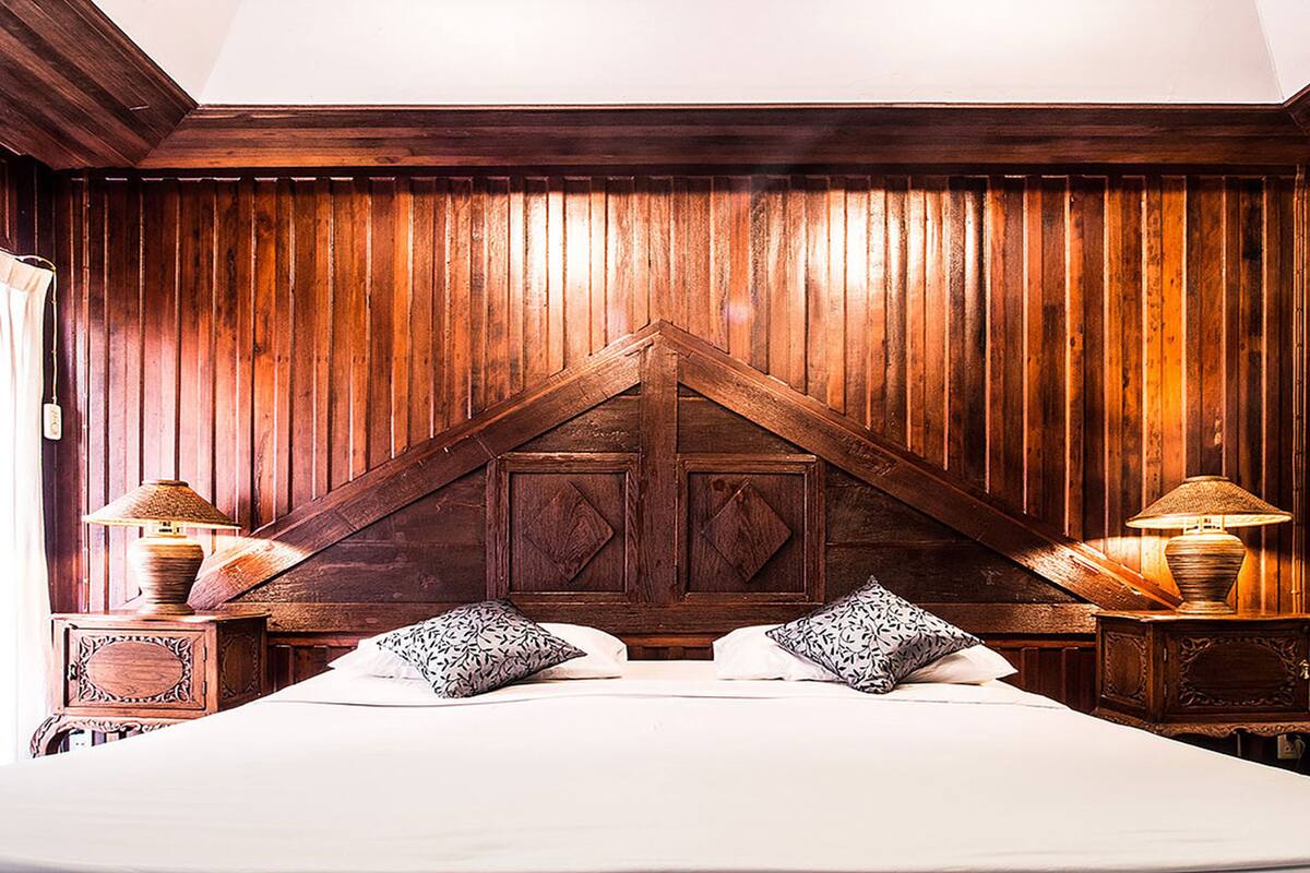 A bedroom with a wooden headboard, two bedside tables with lamps, and patterned pillows.
